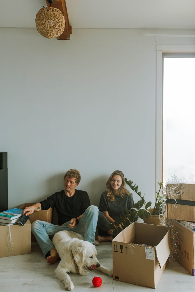 A couple sitting with their dog and unpacked boxes in a new home.