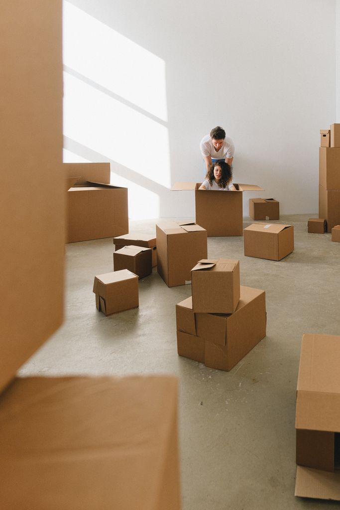 A man and woman playing in cardboard boxes during a move. Bright, indoor setting.