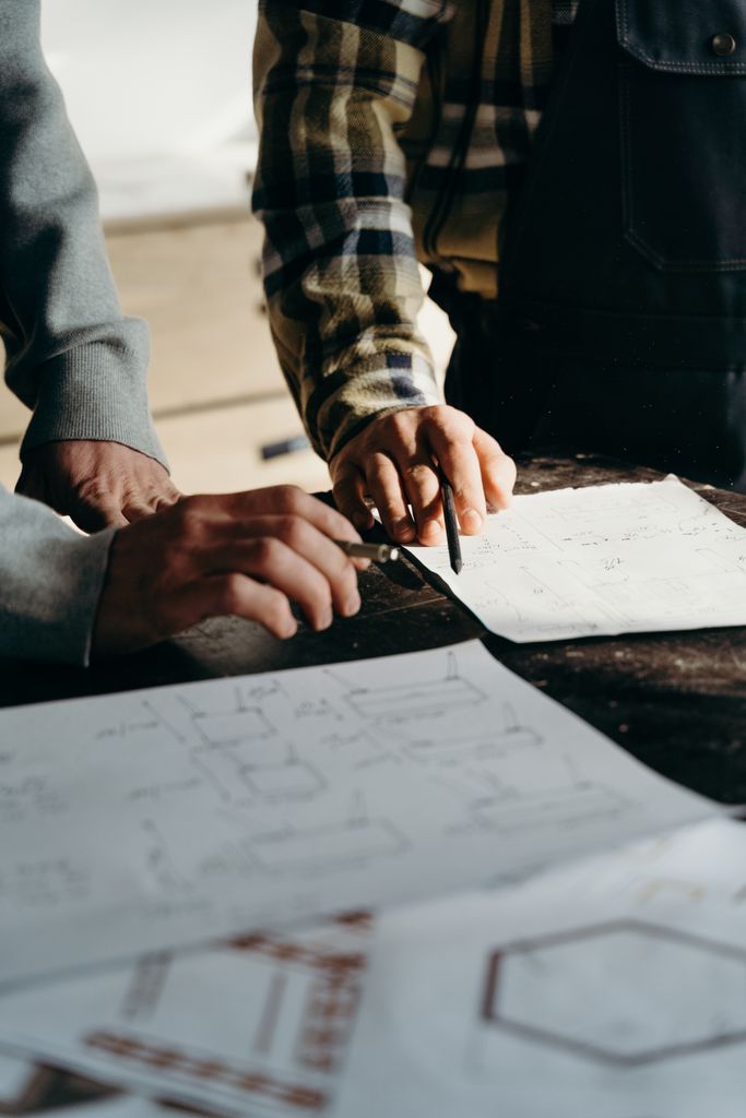 Close-up of hands working on blueprints in a workshop environment.
