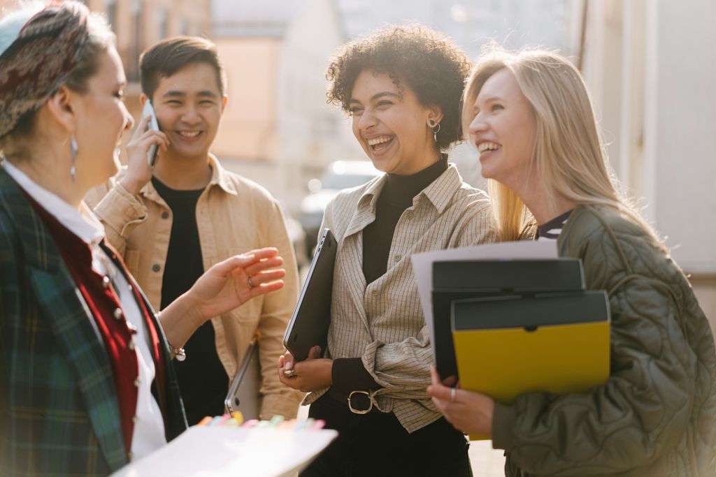 Group of adults laughing and conversing outdoors, capturing a joyful and diverse work environment.