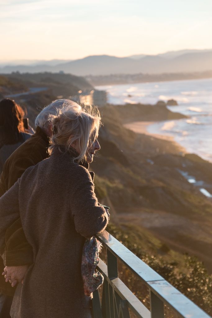 Senior couple holding hands while viewing the stunning sunset over the coastline in Biarritz, France.
