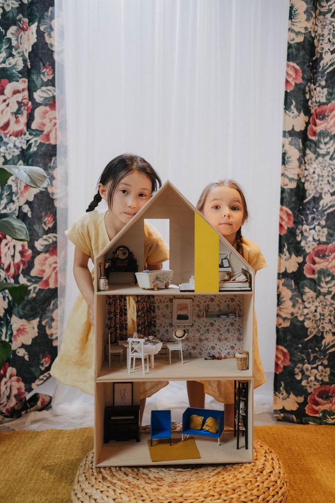 Two young girls engaged in imaginative play with a dollhouse in a cozy indoor setting.